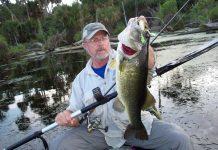 A middle aged man holds up a large bass while fishing from a kayak